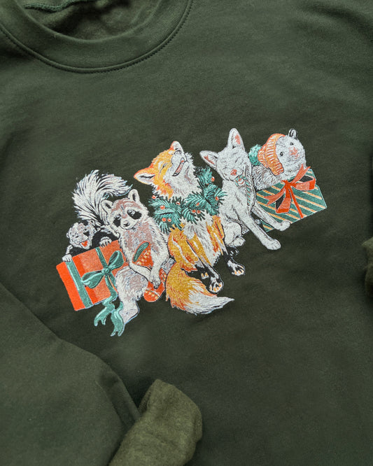 Green sweatshirt with embroidered design of cartoon animals and presents on a wooden surface.